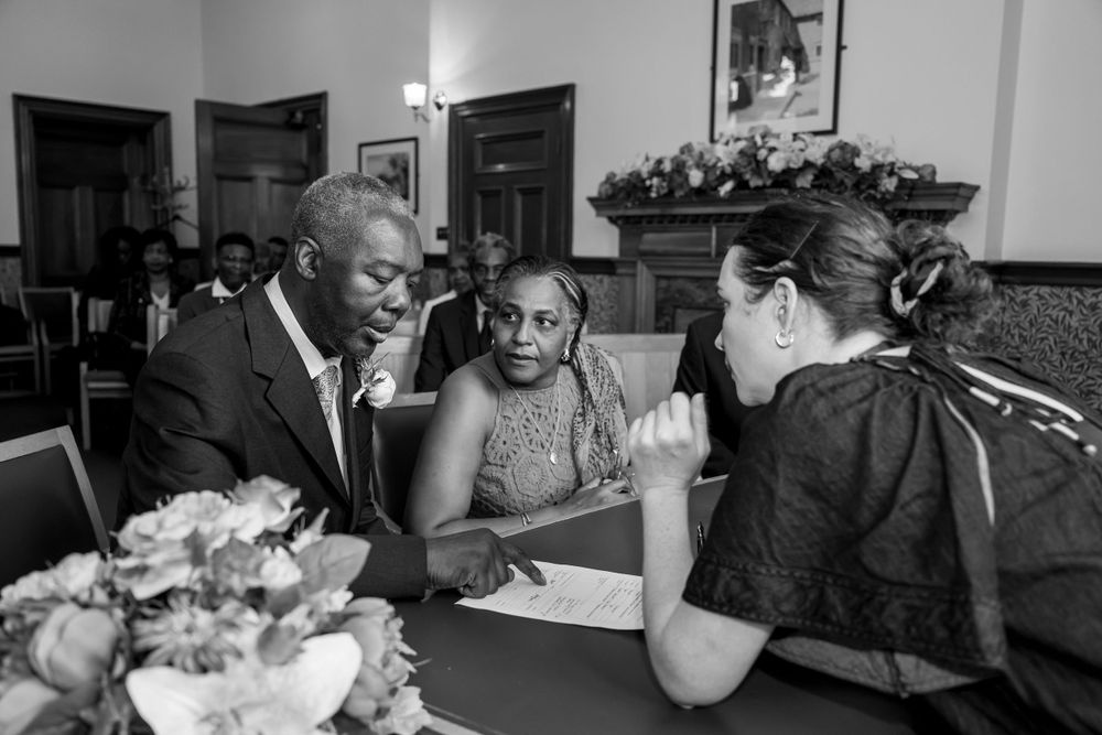 Three people sit at a table having a serious discussion while reviewing paperwork together in black and white.