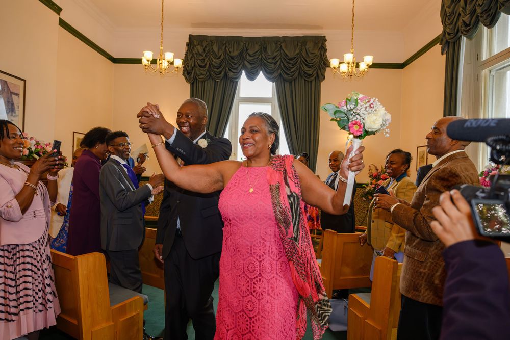 Celebratory moment with people dancing and clapping in a church or chapel with green drapes and chandelier lighting.