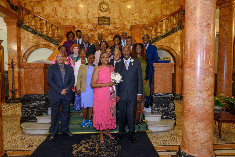 Large group standing together on elegant marble staircase with ornate architectural details and columns in formal attire.