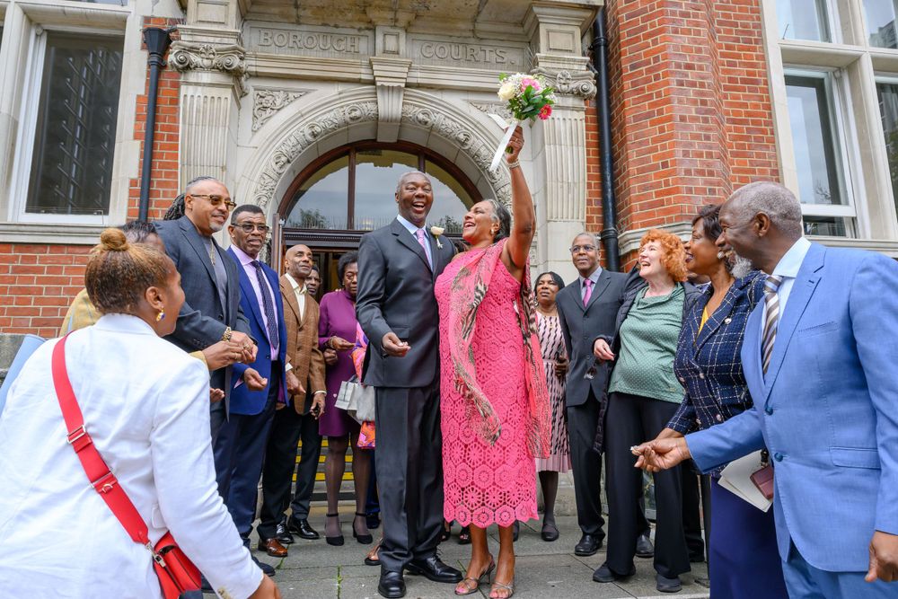 A large crowd of formal-dressed people gathered outside a brick building entrance during a special event.