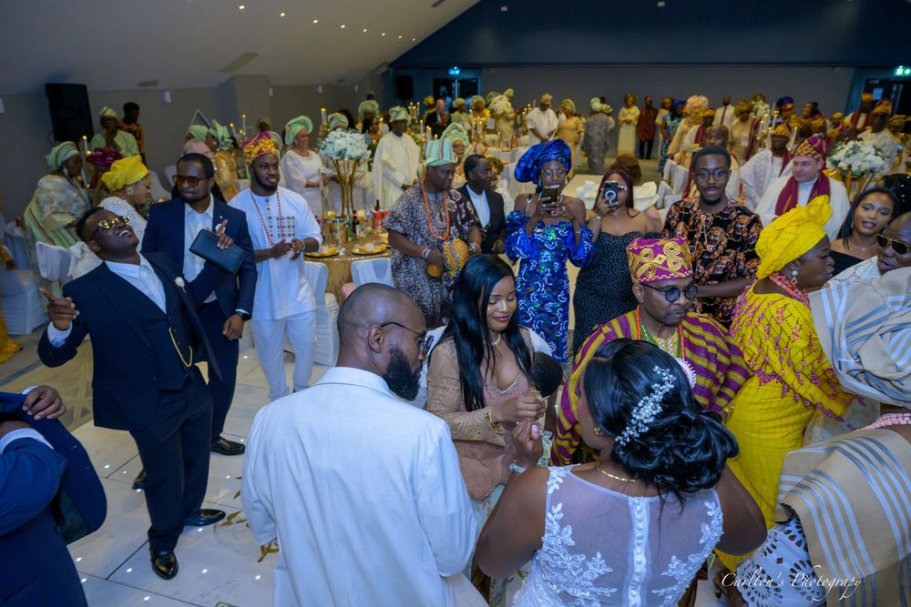 Crowd of wedding guests in colorful traditional African attire dancing and celebrating at an indoor reception.
