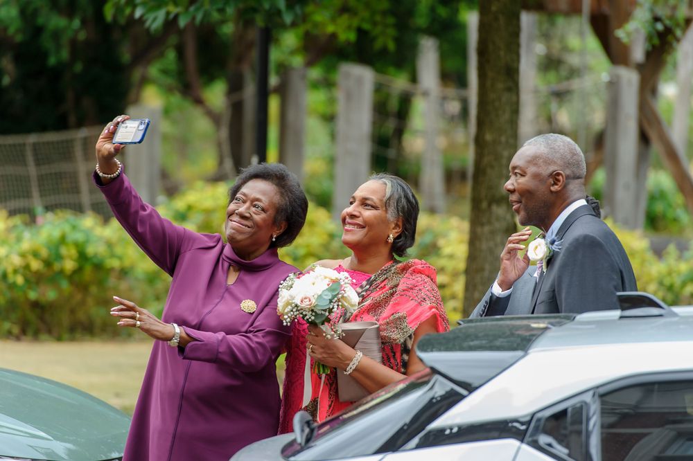 Group taking cheerful selfies outdoors near parked cars.