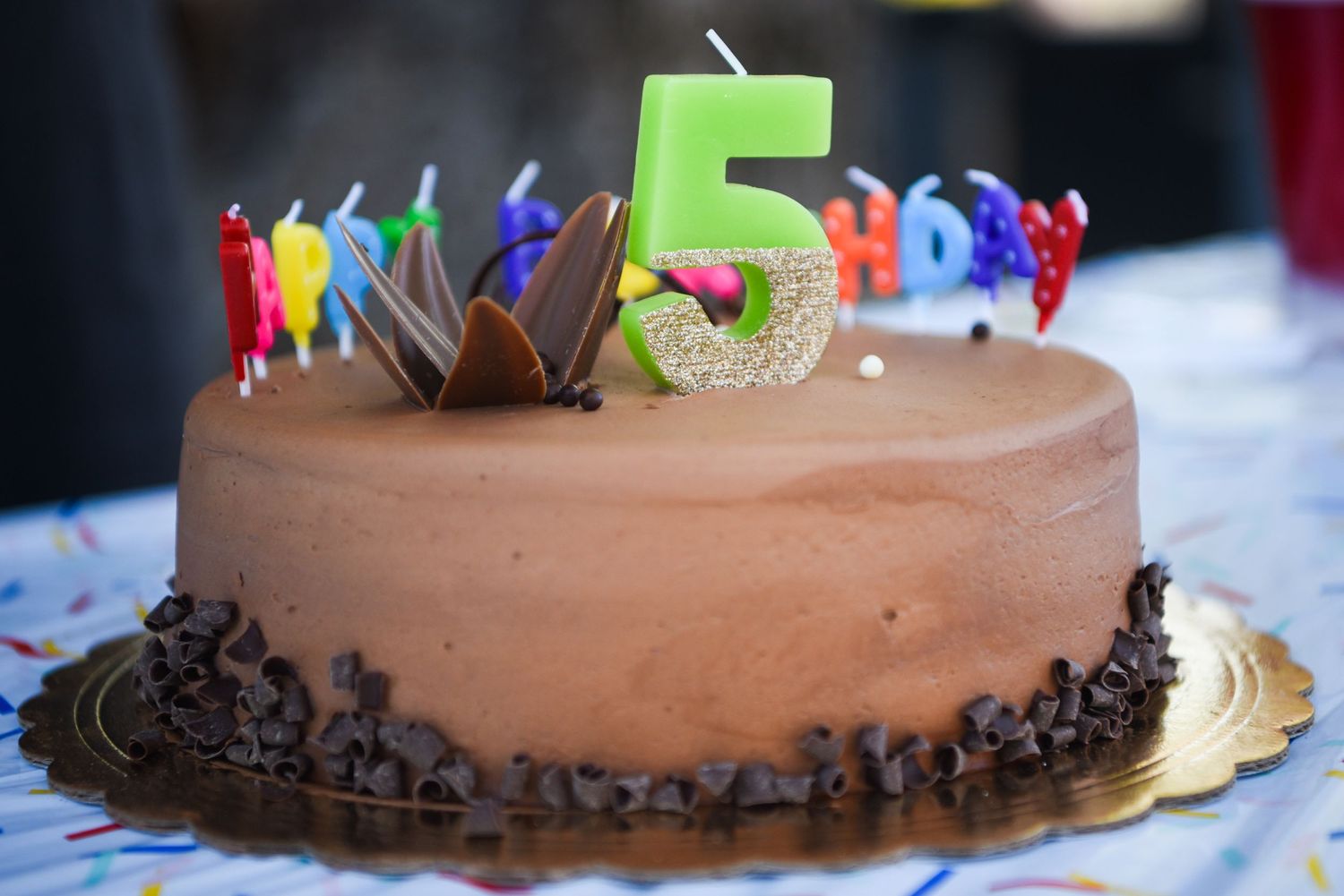 Photograph of a birthday cake decorated with a green number 5 candle and colorful candles on top.