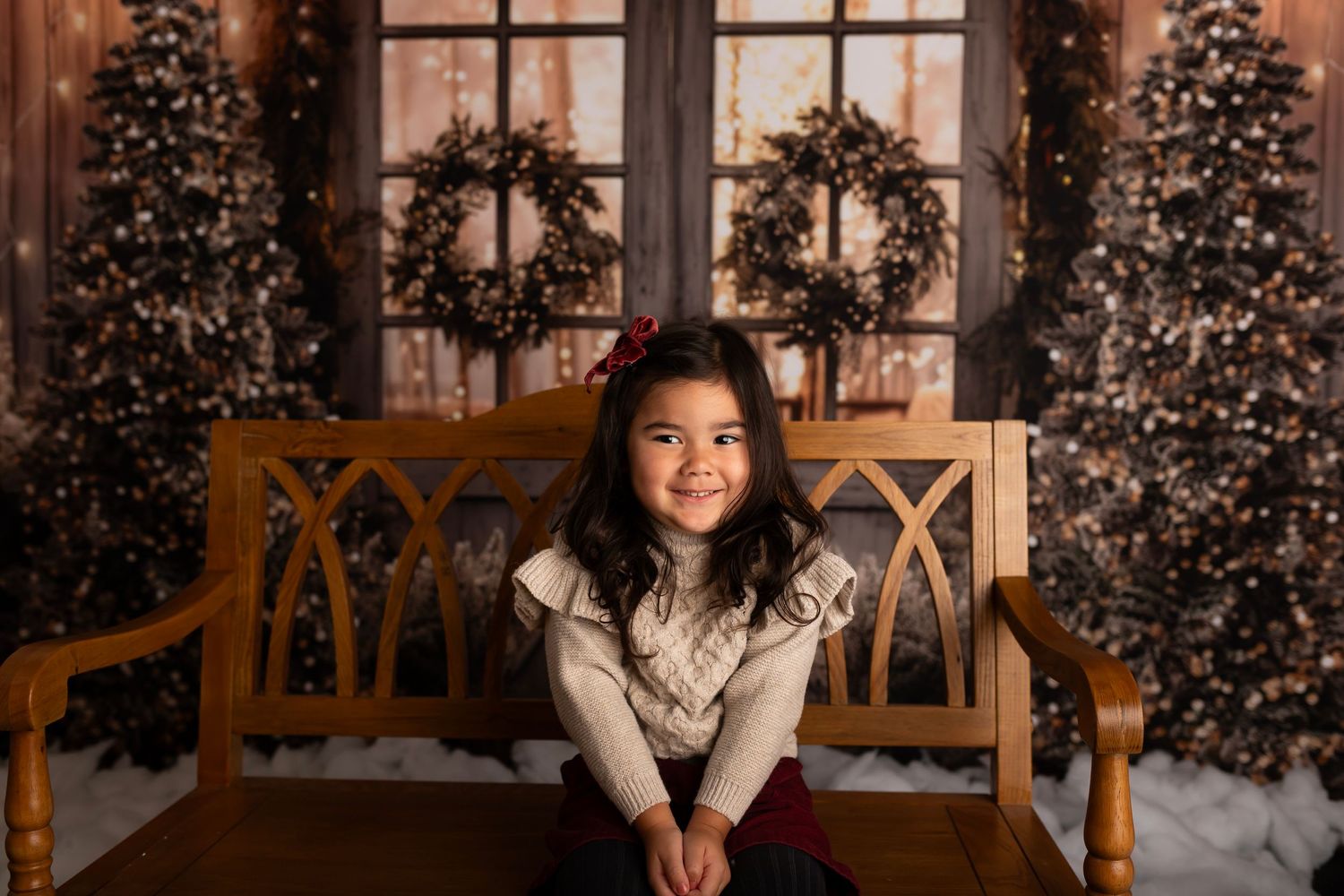 Young child sitting on wooden bench with Christmas decorations and trees in background.