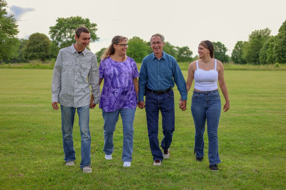 Four people walking together across a green field on a cloudy summer day.