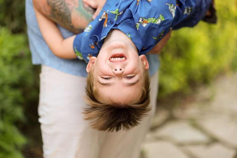 Playful upside down portrait of a laughing child against a blurred green background.