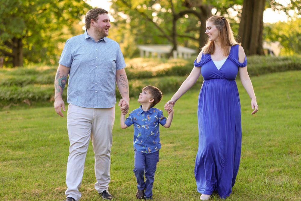 Family takes a sunny walk together in a park with green trees in the background.