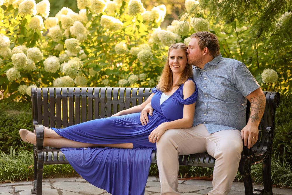Couple sits together on wooden bench surrounded by blooming yellow flowers in garden.