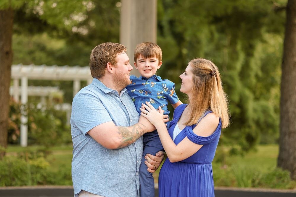 Parents share tender moment with young child in outdoor garden setting.