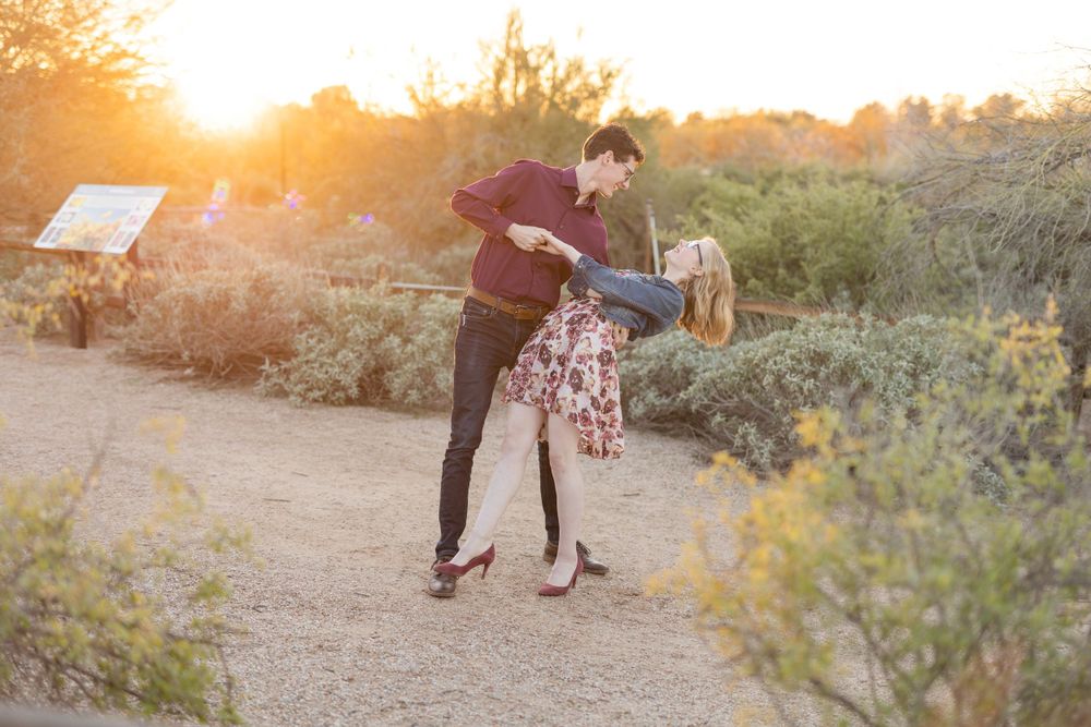 Joyful couple dancing in desert landscape during sunset photoshoot.
