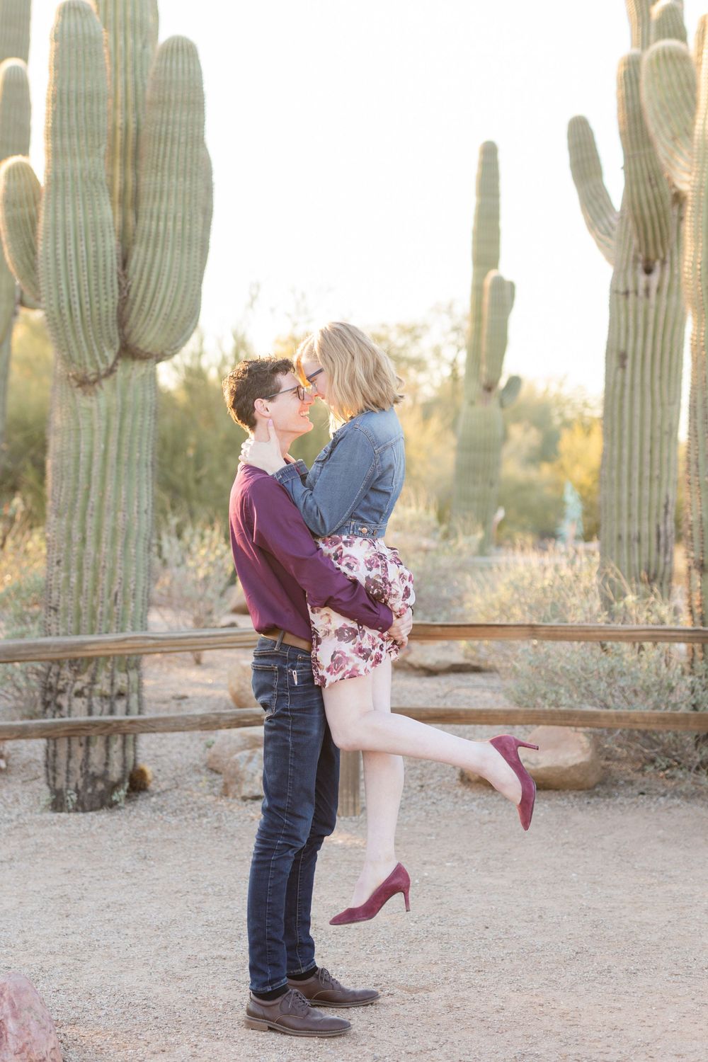 Playful couple shares romantic moment among saguaro cacti during sunset photo session.
