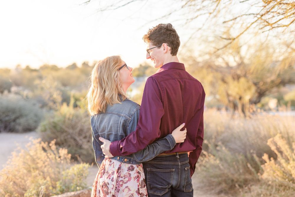 Couple embraces on desert path with golden sunlight filtering through desert brush.