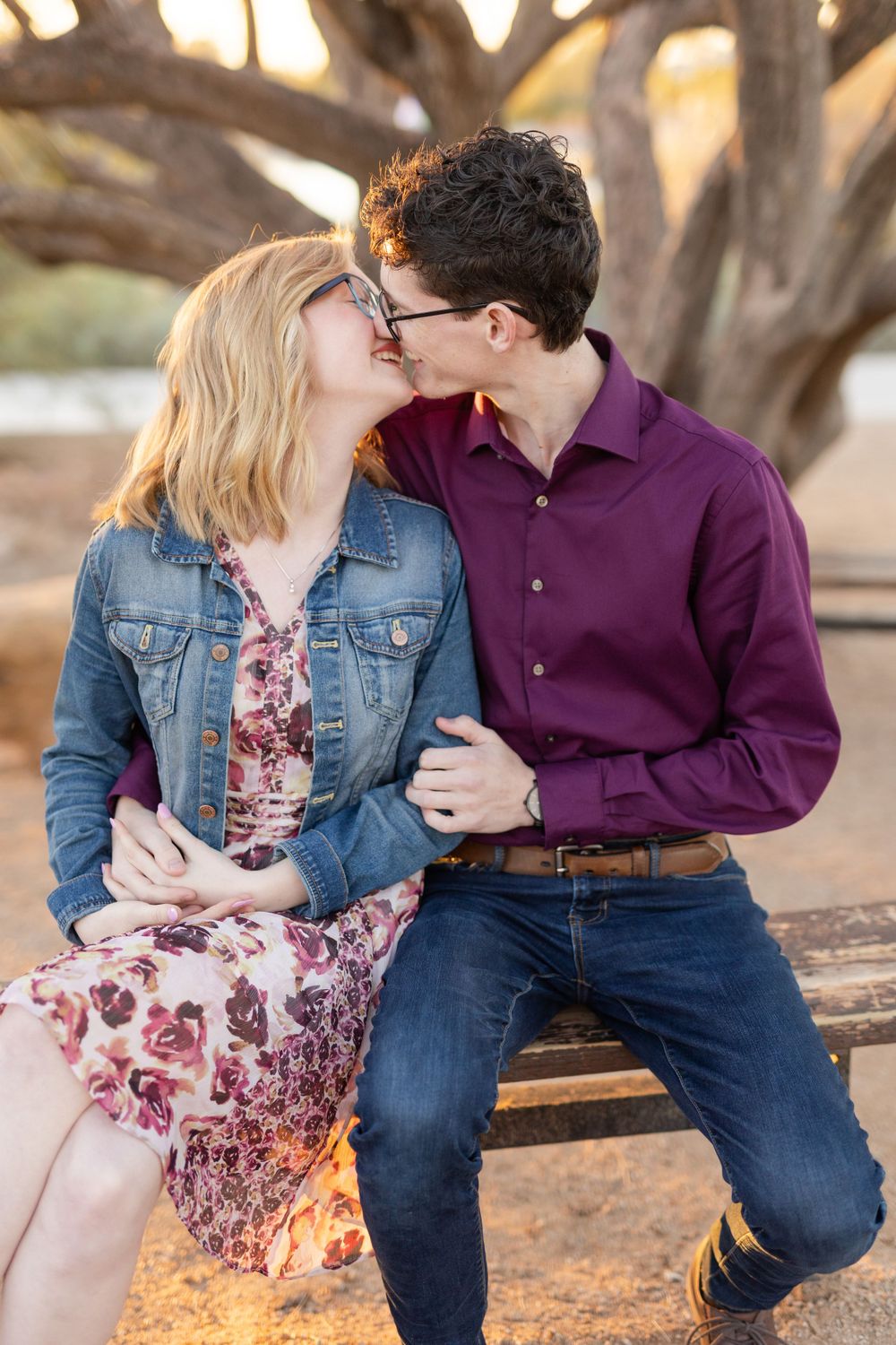 Intimate couple moment captured on park bench with desert trees in background.