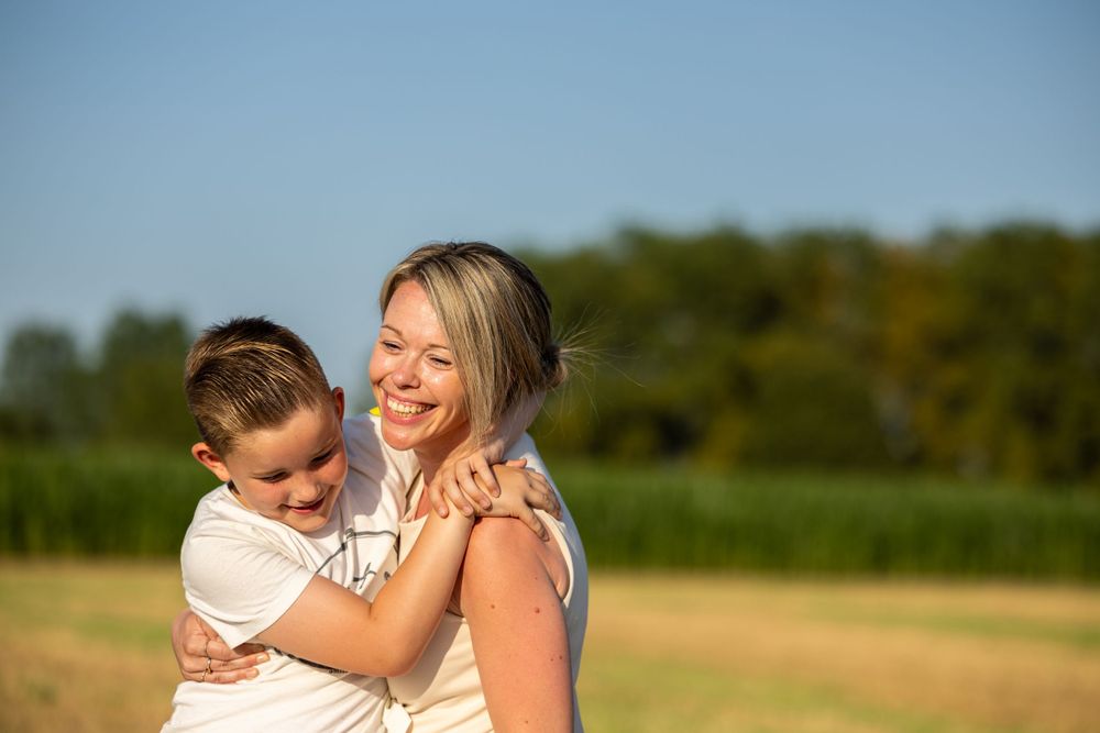 Mother and child share warm embrace in sunlit summer field.