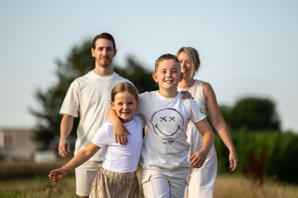 Family wearing coordinated white outfits smile together outdoors in evening light.