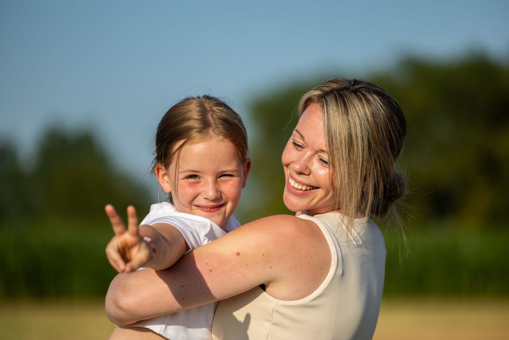 Mother and child share playful moment outdoors in summer sunshine.