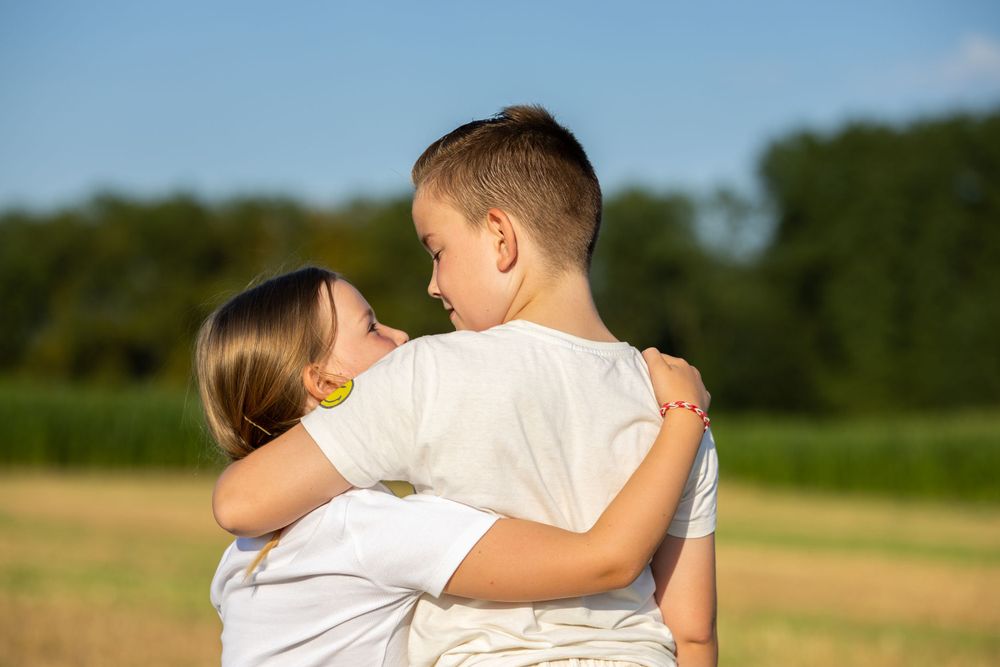 Two people sharing an embrace in a sunny field with trees in the background.