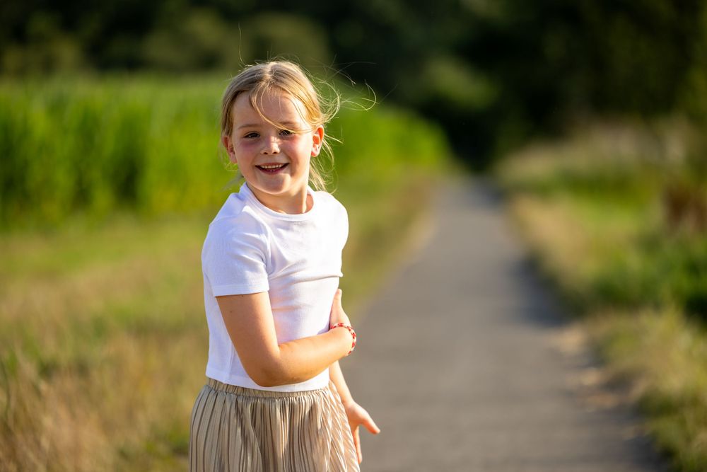 Young person in white shirt standing on a path surrounded by summer greenery.