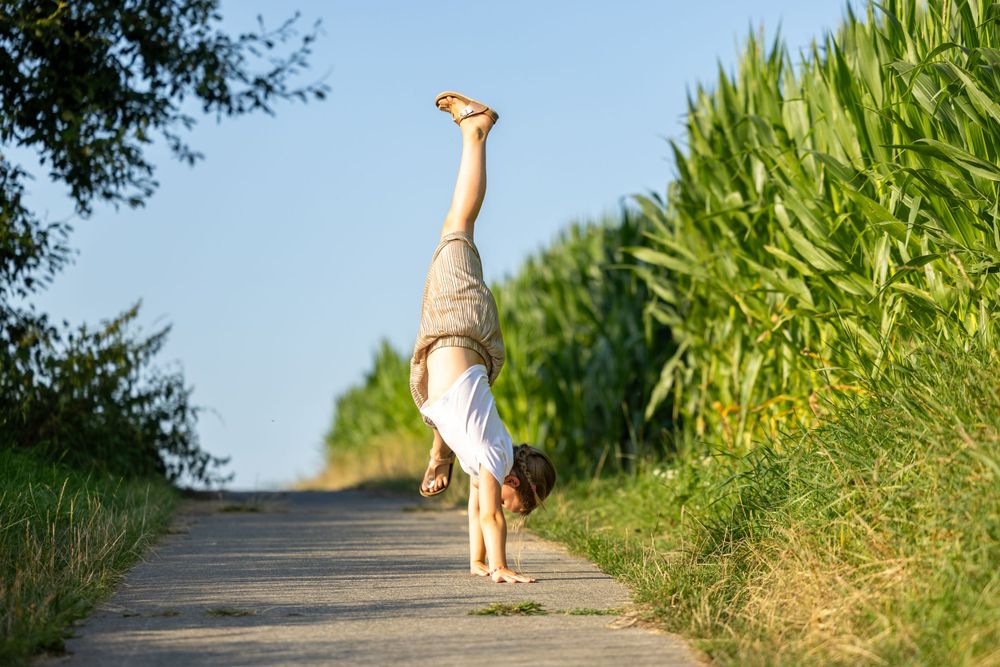 Person doing a handstand on a rural path between green fields.