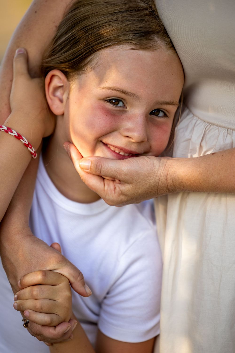 Close up portrait of a child in white shirt being embraced.