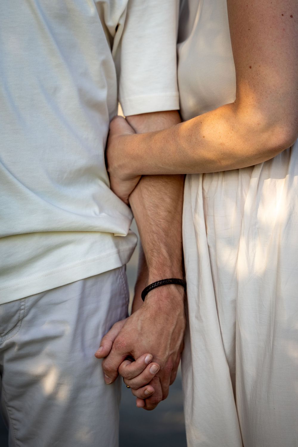 Close-up of hands tenderly clasped together against white clothing.