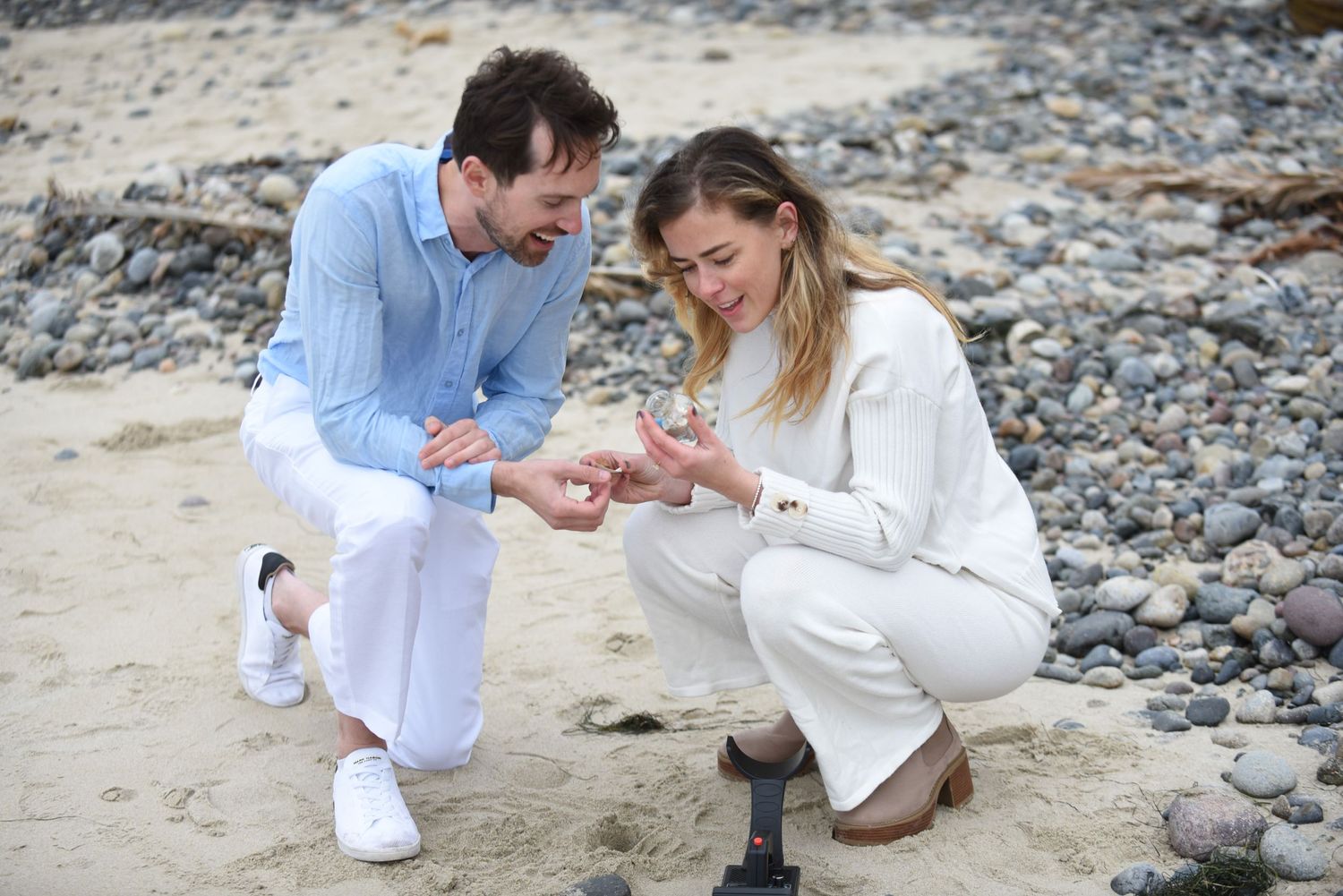 A couple sharing an intimate proposal moment on a rocky beach by the ocean.