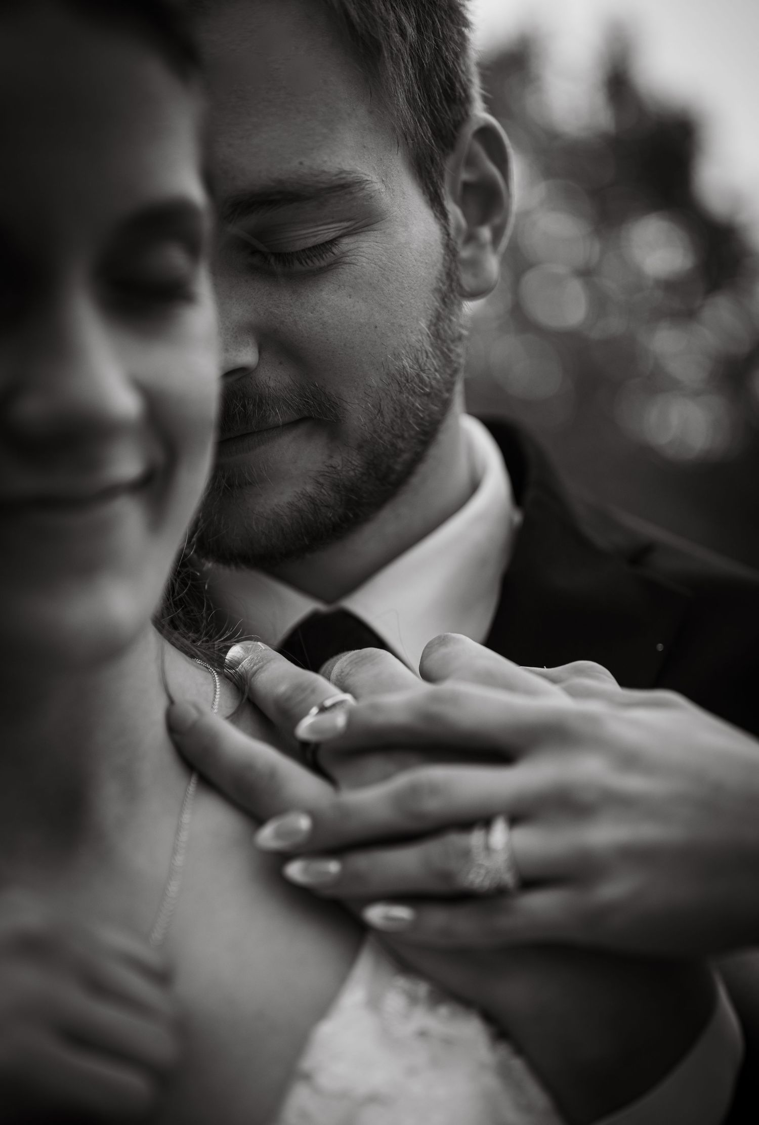 Black and white photo of newlyweds embracing, showing wedding rings on their hands.