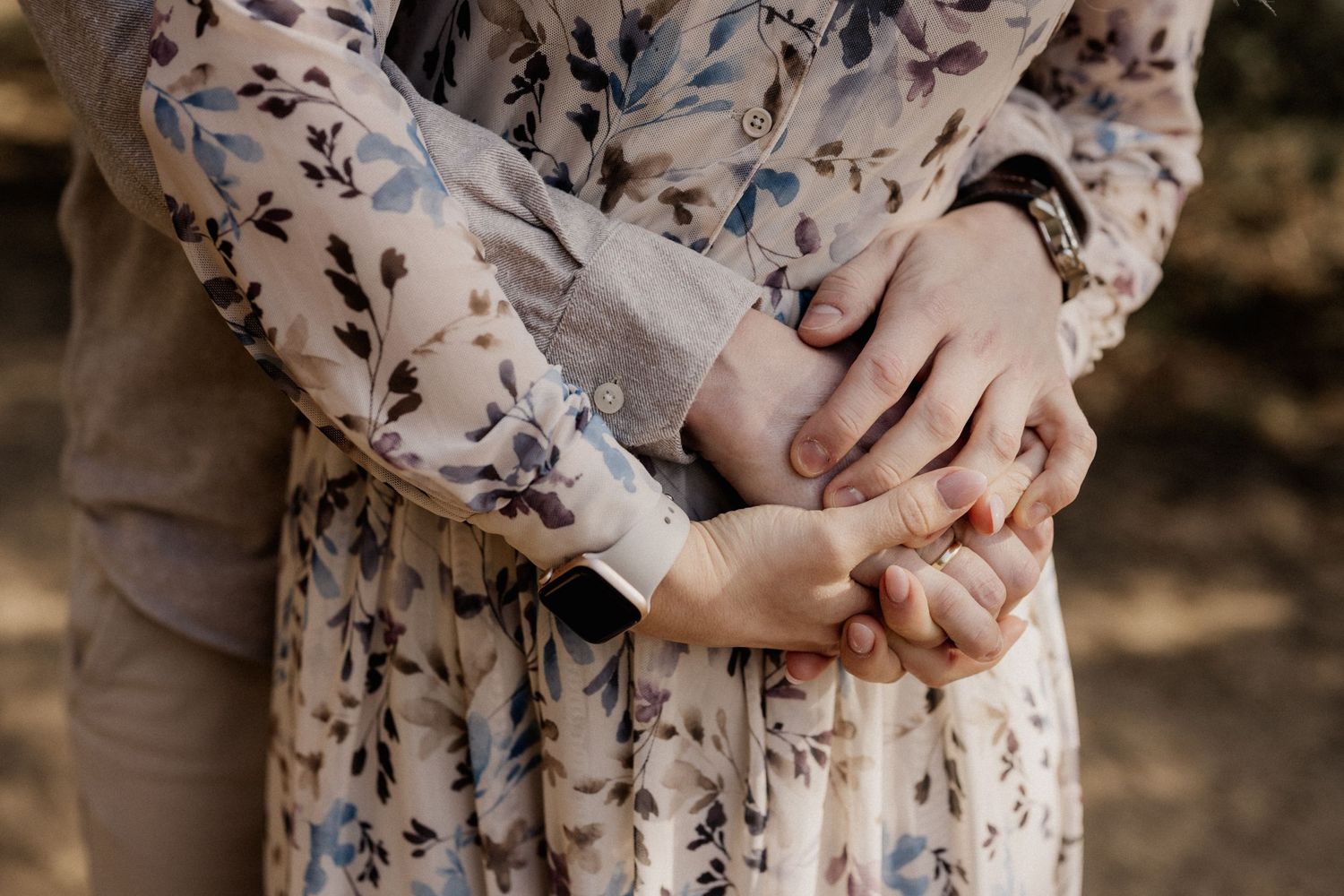 A person in a delicate floral print dress holds their hands together in front of their torso in natural lighting.