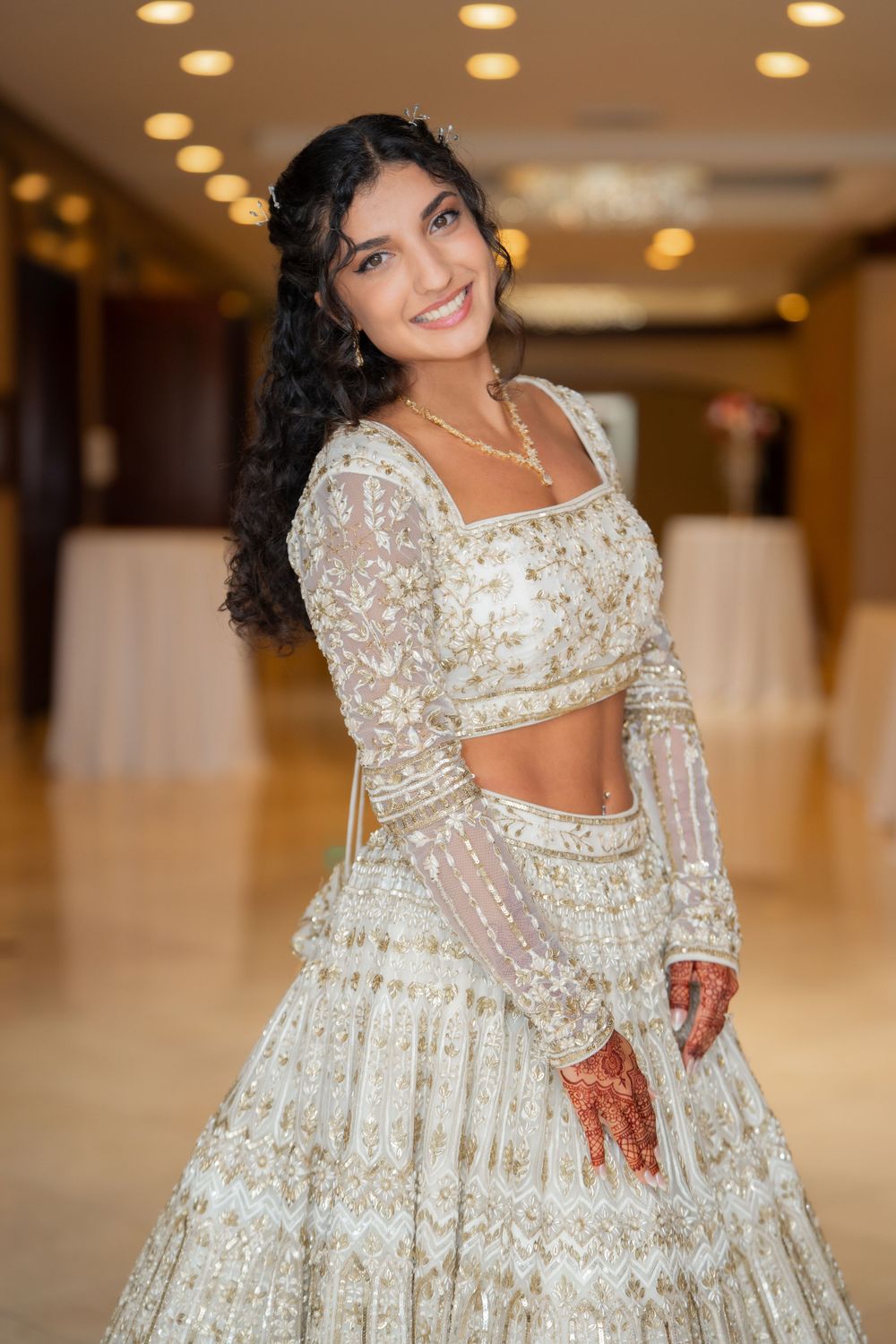 Traditional bride in detailed white and gold lehenga with henna adorned hands.