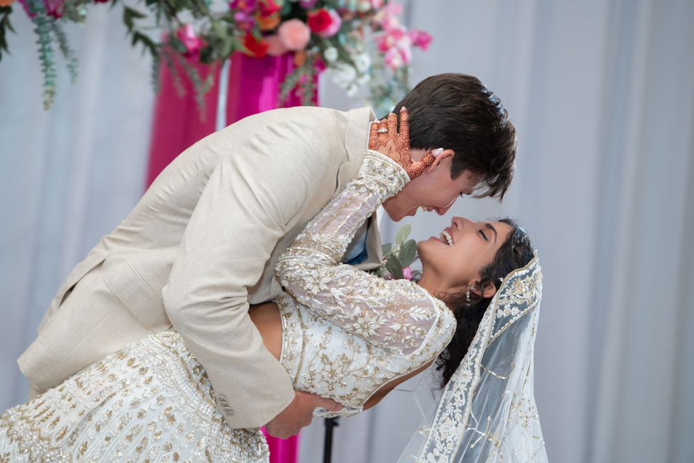 A romantic wedding dip pose with the couple in white attire against a floral backdrop and white draping.