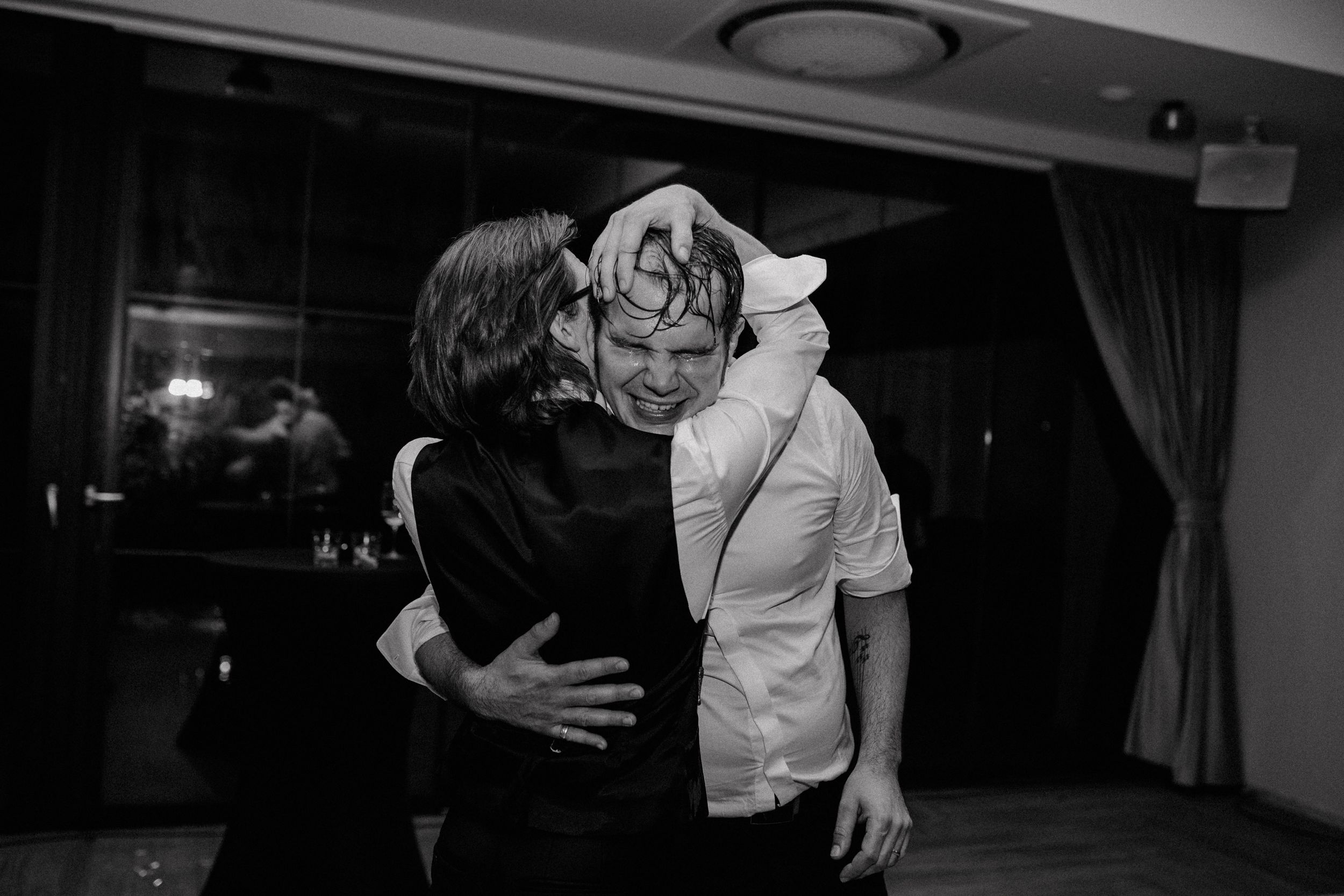 Black and white photo of the groom embracing his friend with intense emotion during wedding party in Zagreb..