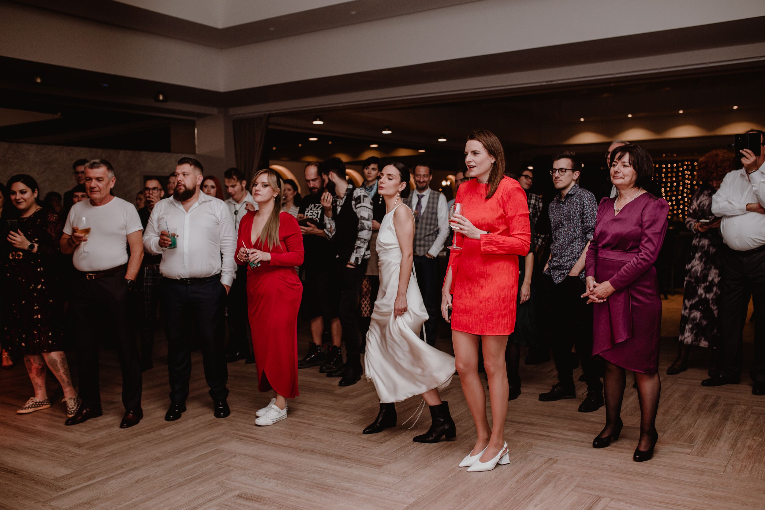 Wedding guests joyfully listening as the groom and best man perform with the band, with the bride smiling and enjoying.