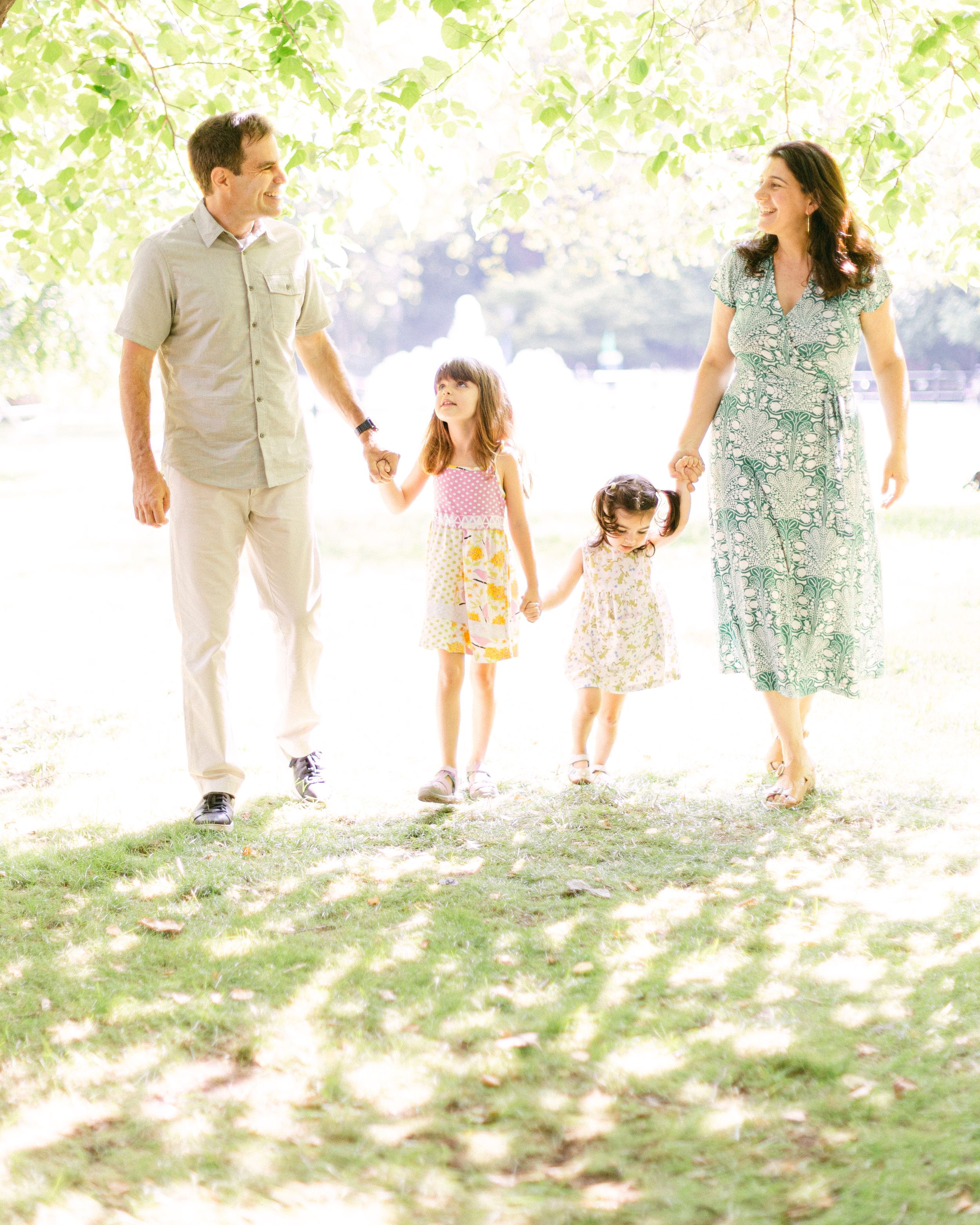 A family holds hands while walking together outdoors in a sunlit park setting wearing coordinated spring outfits.