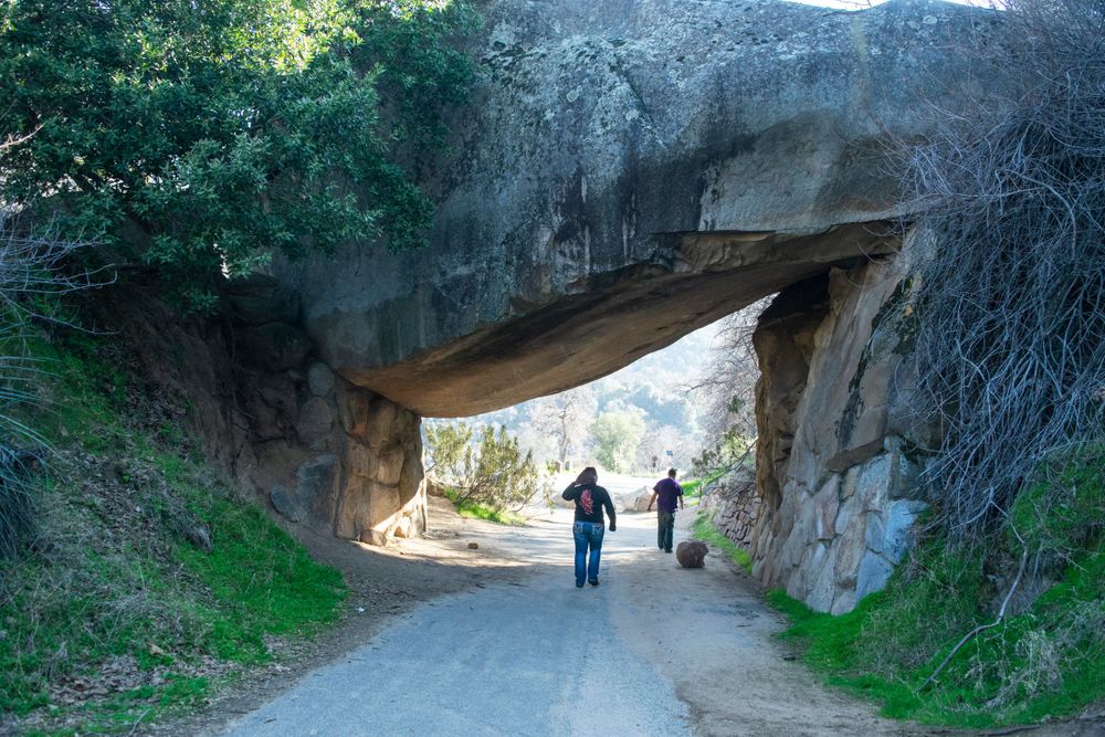 Natural stone arch formation spanning over hiking trail with people walking underneath.