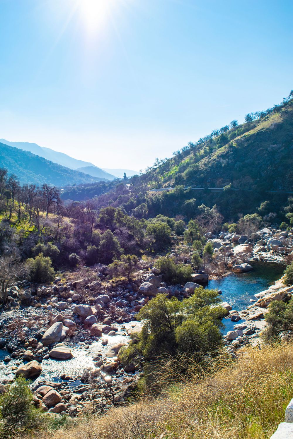 Rocky river valley with bright blue pools of water winding through mountainous terrain on sunny day.