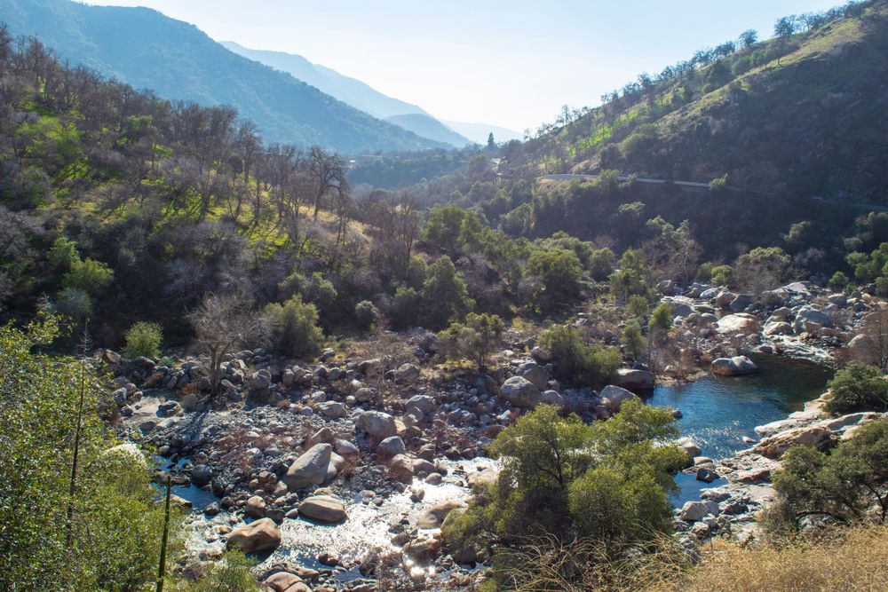 Mountain stream flows through rocky terrain with blue pools of water in rugged valley landscape.