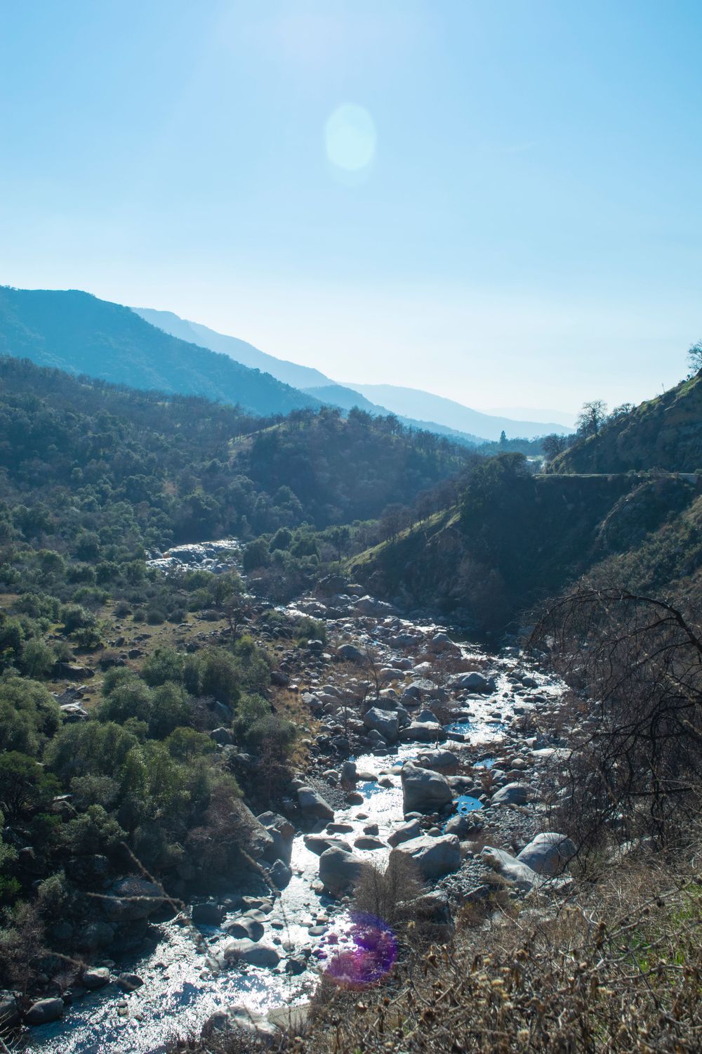 Mountain stream cascades over rocks through steep canyon under bright sunny sky.