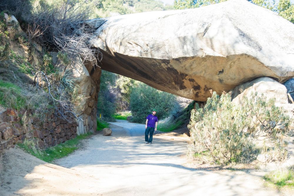 Natural rock arch forms tunnel over hiking trail through mountainous terrain.