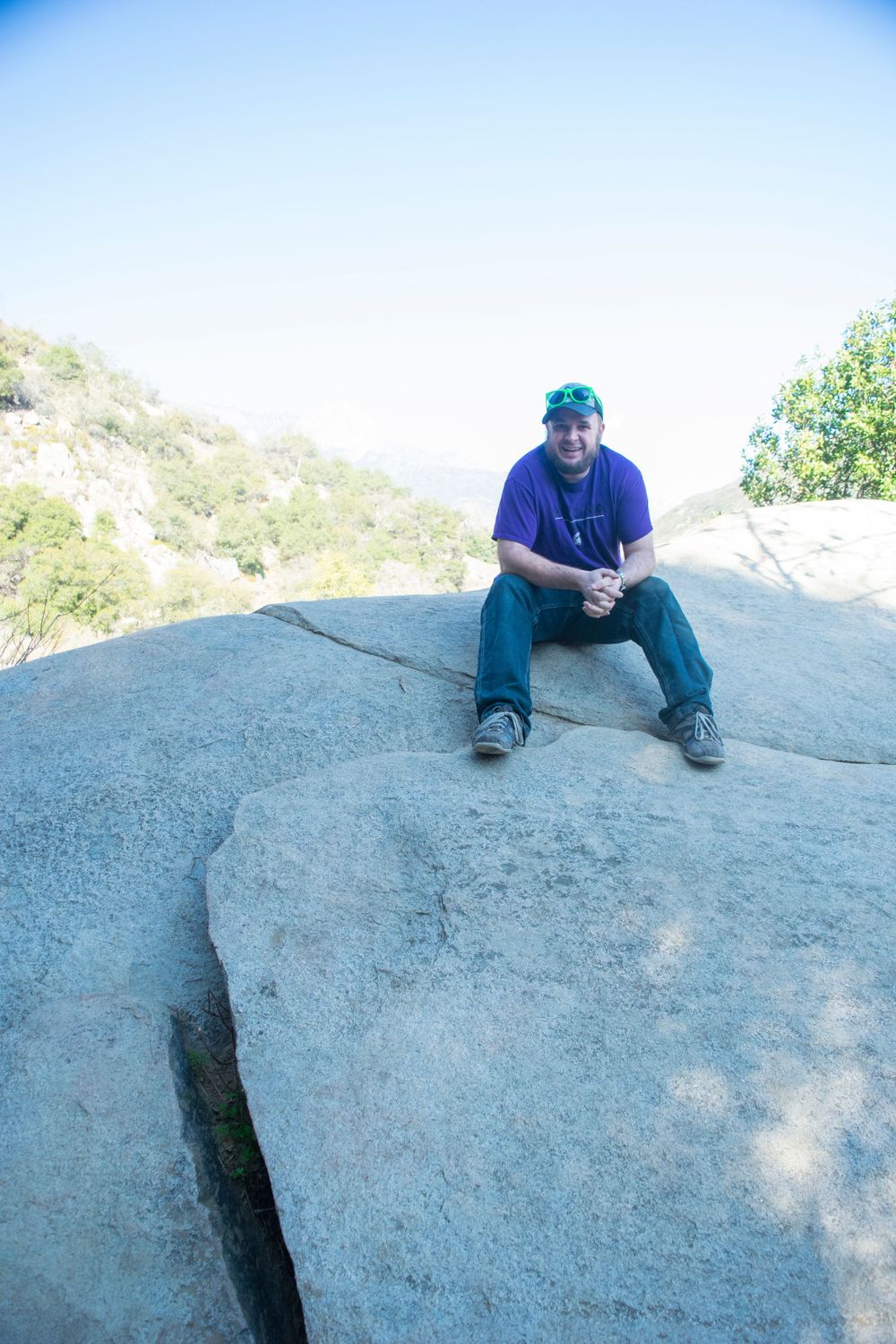 Hiker sitting on large granite boulder overlooking scenic mountain vista on sunny day.