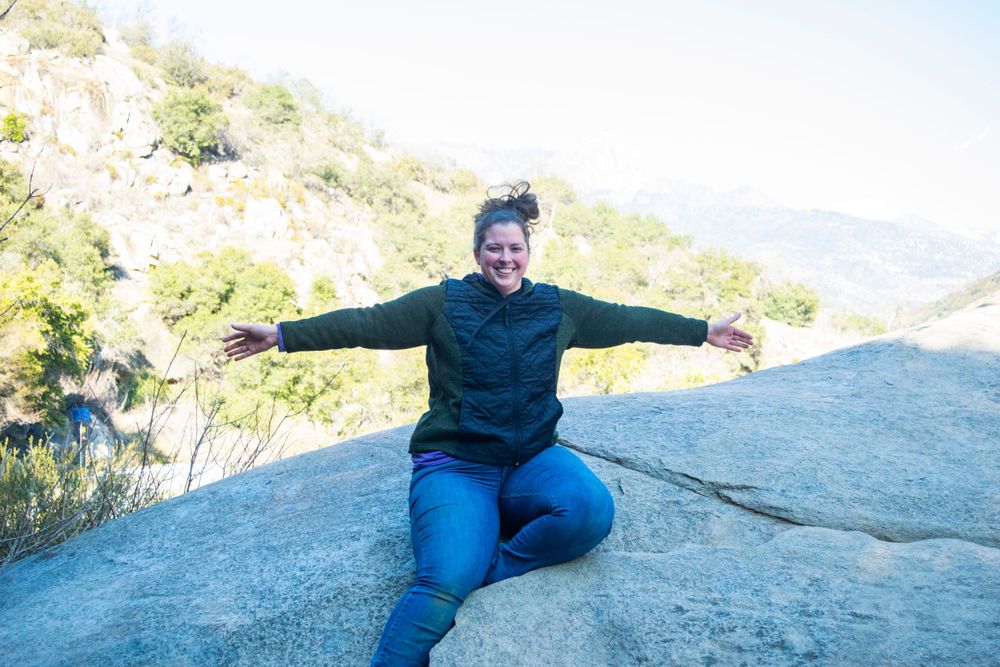 Person enjoying mountain views while sitting spread-eagled on large rock formation.