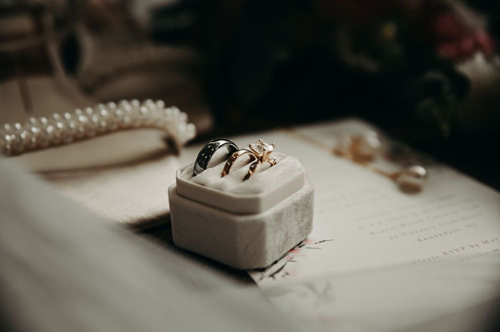 Wedding detail shot showing rings and jewelry boxes arranged on white fabric.
