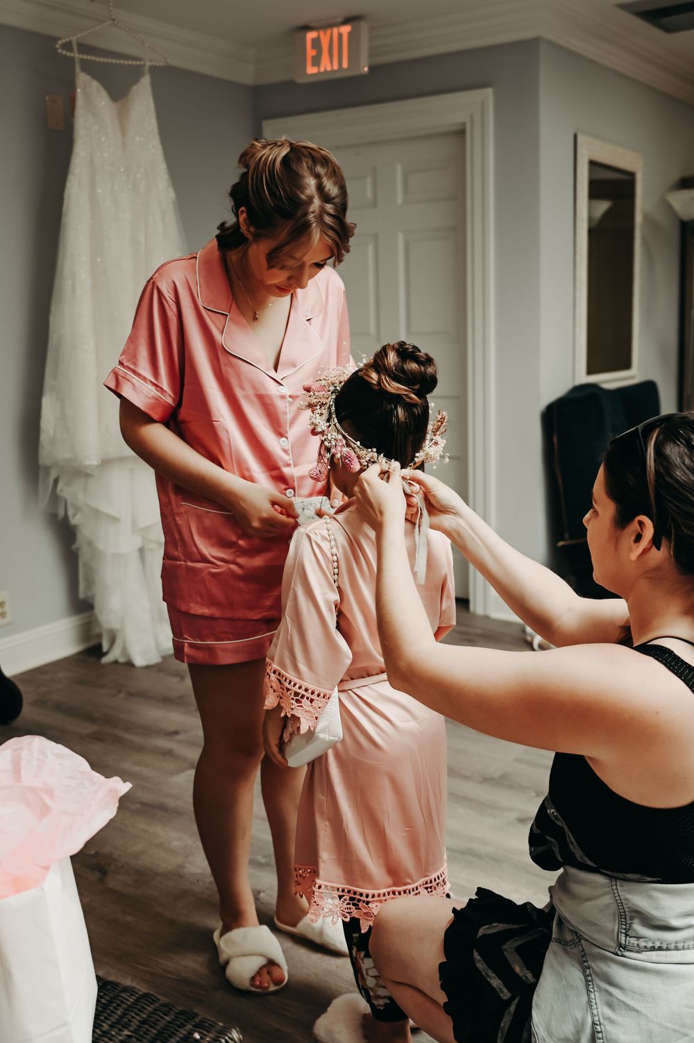 Wedding preparation scene showing pink robes and white dress in a bright room.