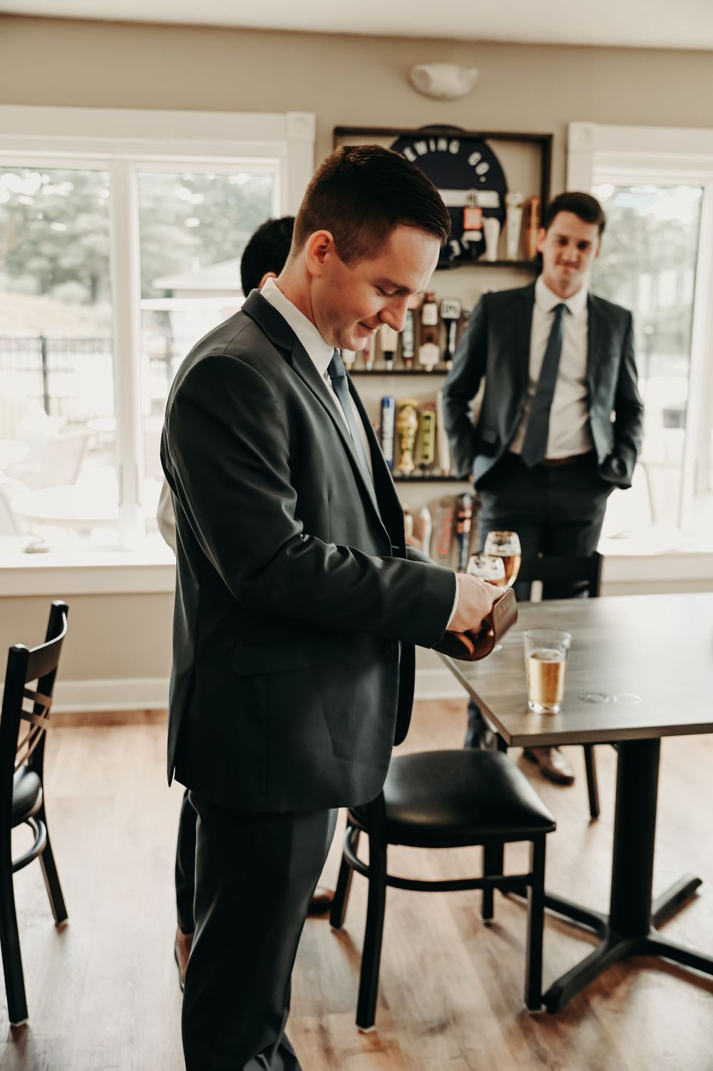 Groomsmen in dark suits share drinks and laughter during pre-wedding preparations.