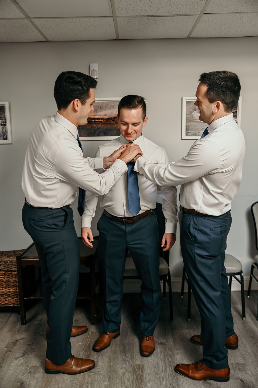 Groomsmen helping each other get ready in formal attire.
