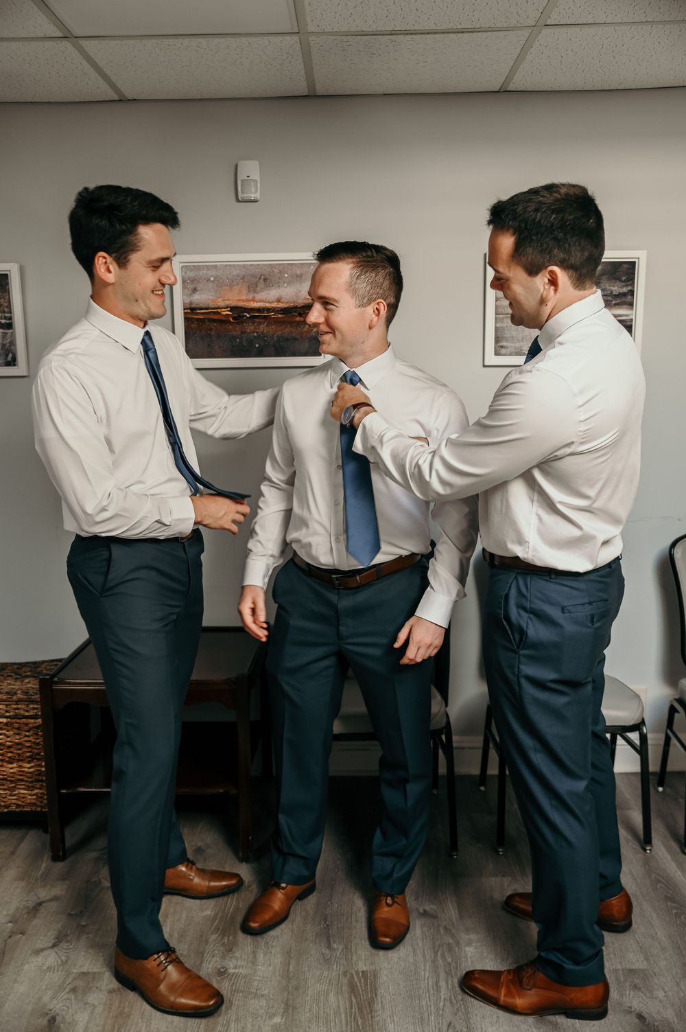 Groomsmen adjusting each other's suits and ties before the wedding.