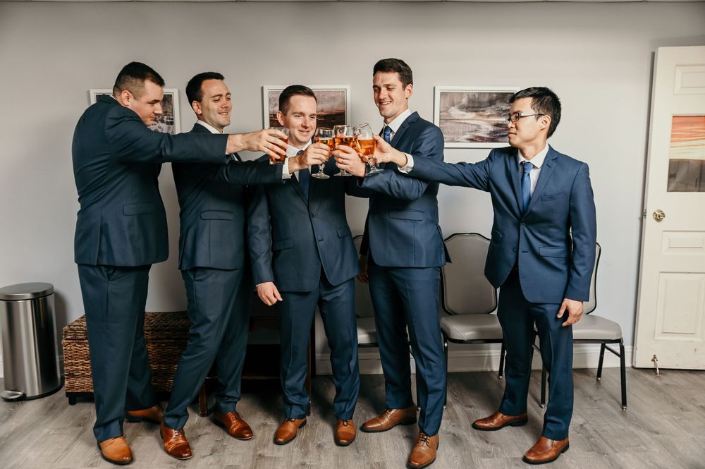 Groomsmen lined up against wall share laughs during pre-wedding preparations.