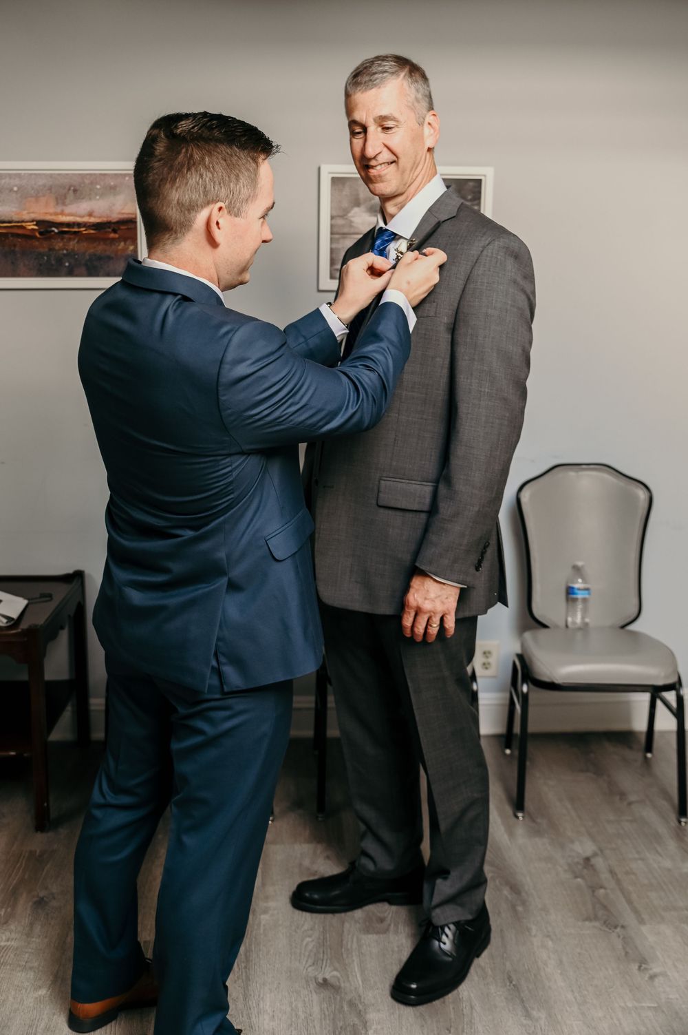 Two people in formal attire adjust clothing details before an event.
