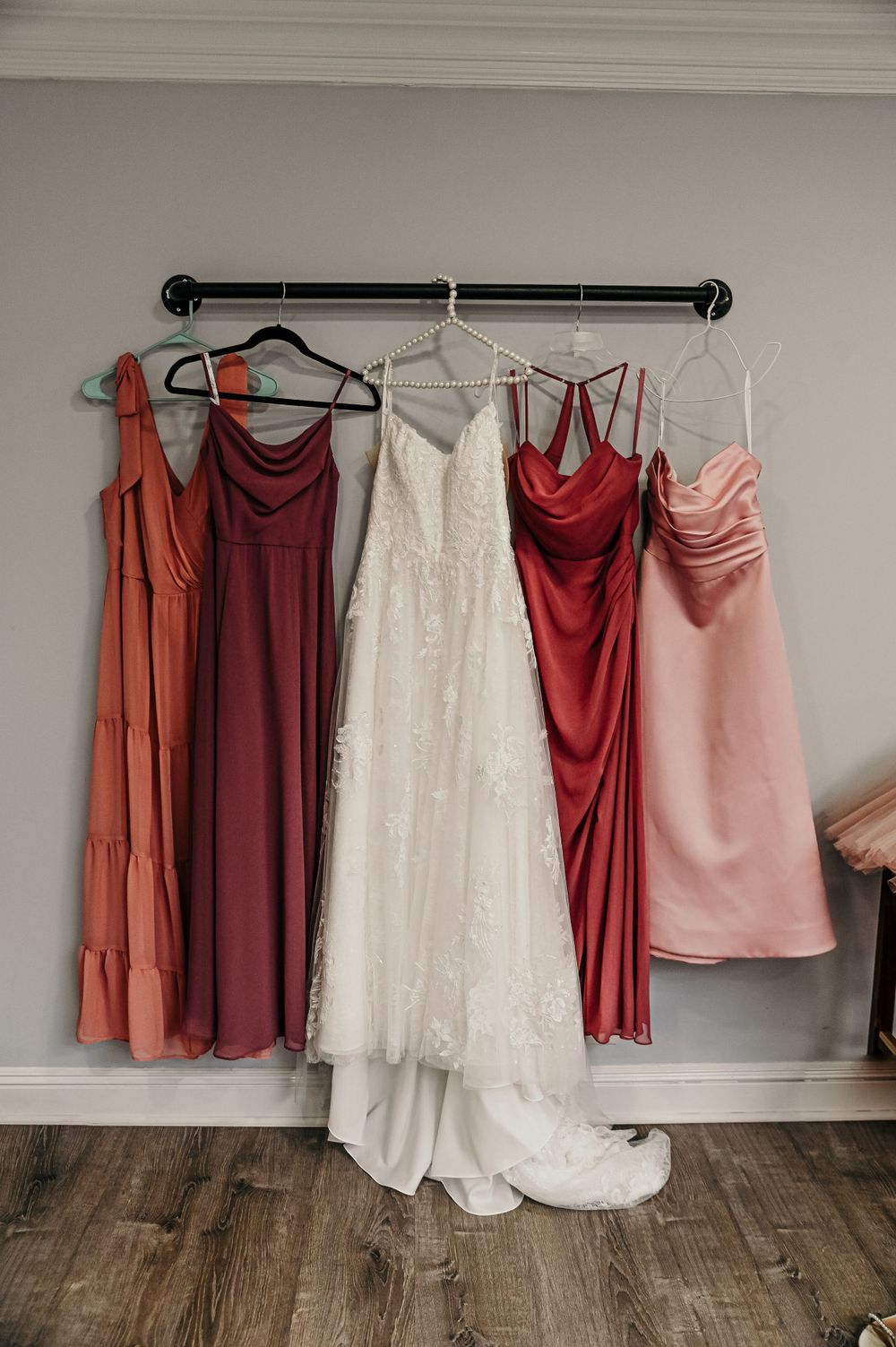 Coordinated burgundy, coral and white bridesmaid dresses hanging on a rack.