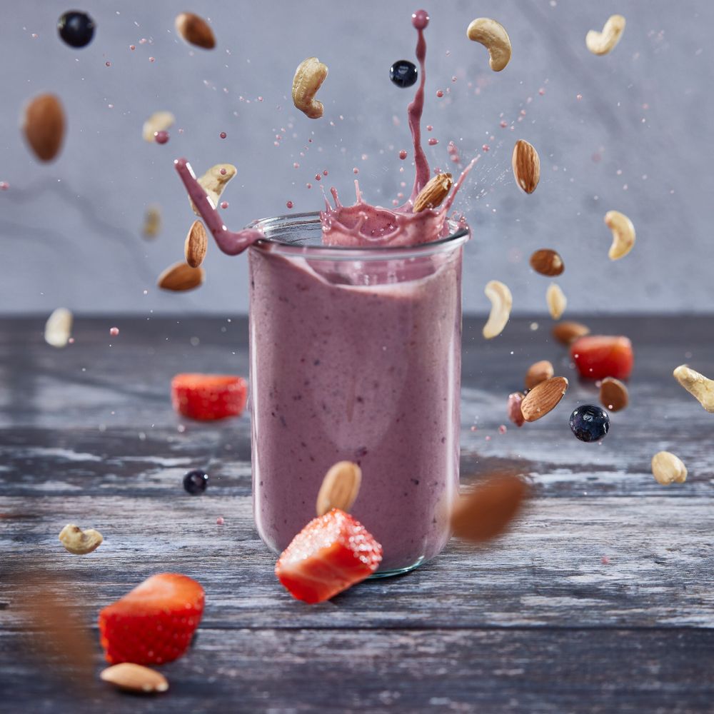 A smoothie exploding out of a glass with nuts falling all around it