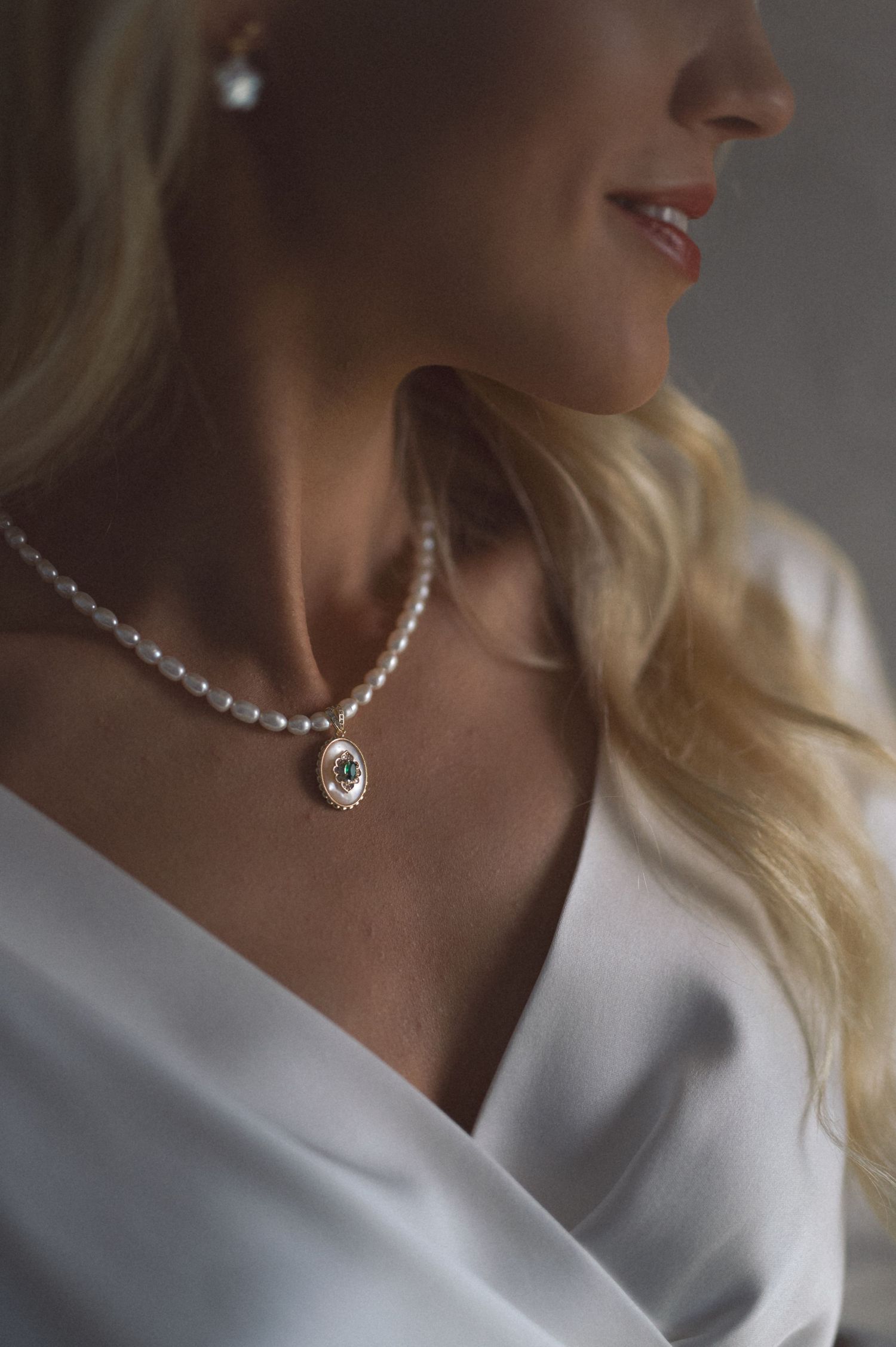 Pearl necklace with pendant worn with white off-shoulder dress in soft lighting.